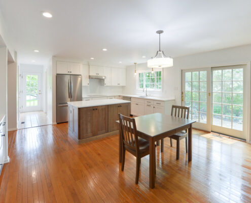 clean modern white eat-in kitchen featuring stained wooden flooring and island cabinets, white wall cabinets with crown molding, white subway tile backsplash, double wall oven